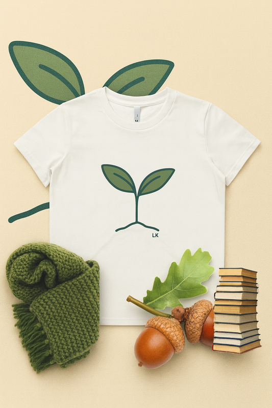 White t-shirt with green leaf design, green fabric, acorn, books on beige background