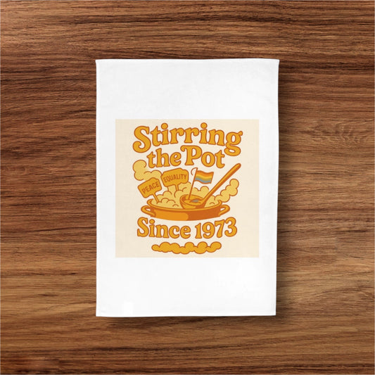 White towel with 'Stirring the Pot Since 1973' design on a wooden surface
