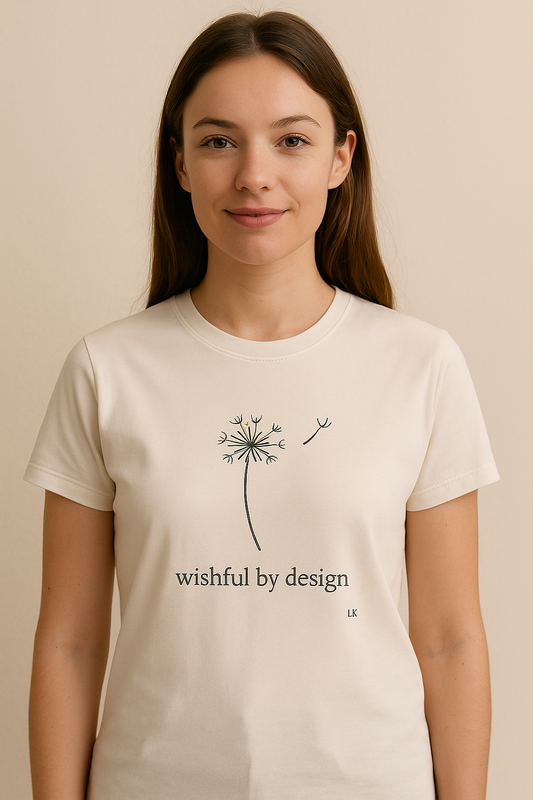 Person wearing a white t-shirt with a dandelion design and 'wishful by design' text on a beige background