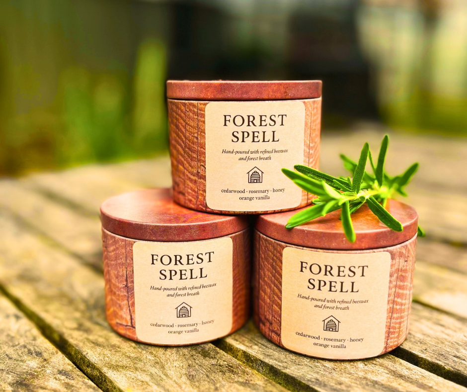 Three 'Forest Spell' candles stacked on a wooden surface with a blurred natural background