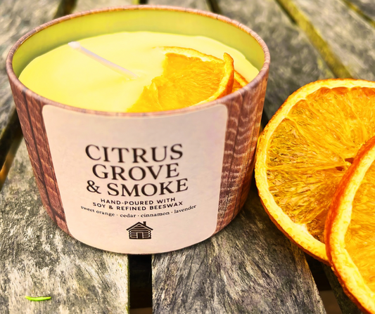 Candle labeled 'Citrus Grove & Smoke' with dried orange slices on a wooden surface