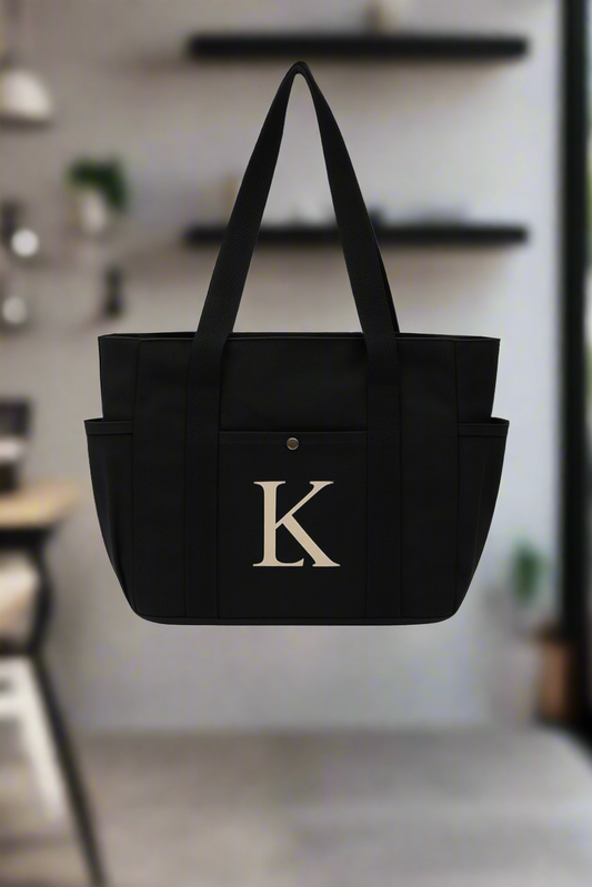 Black tote bag with a gold LK monogram in a blurred indoor setting