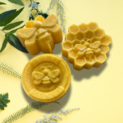 Three yellow bee-themed soap bars on a yellow background with green leaves.