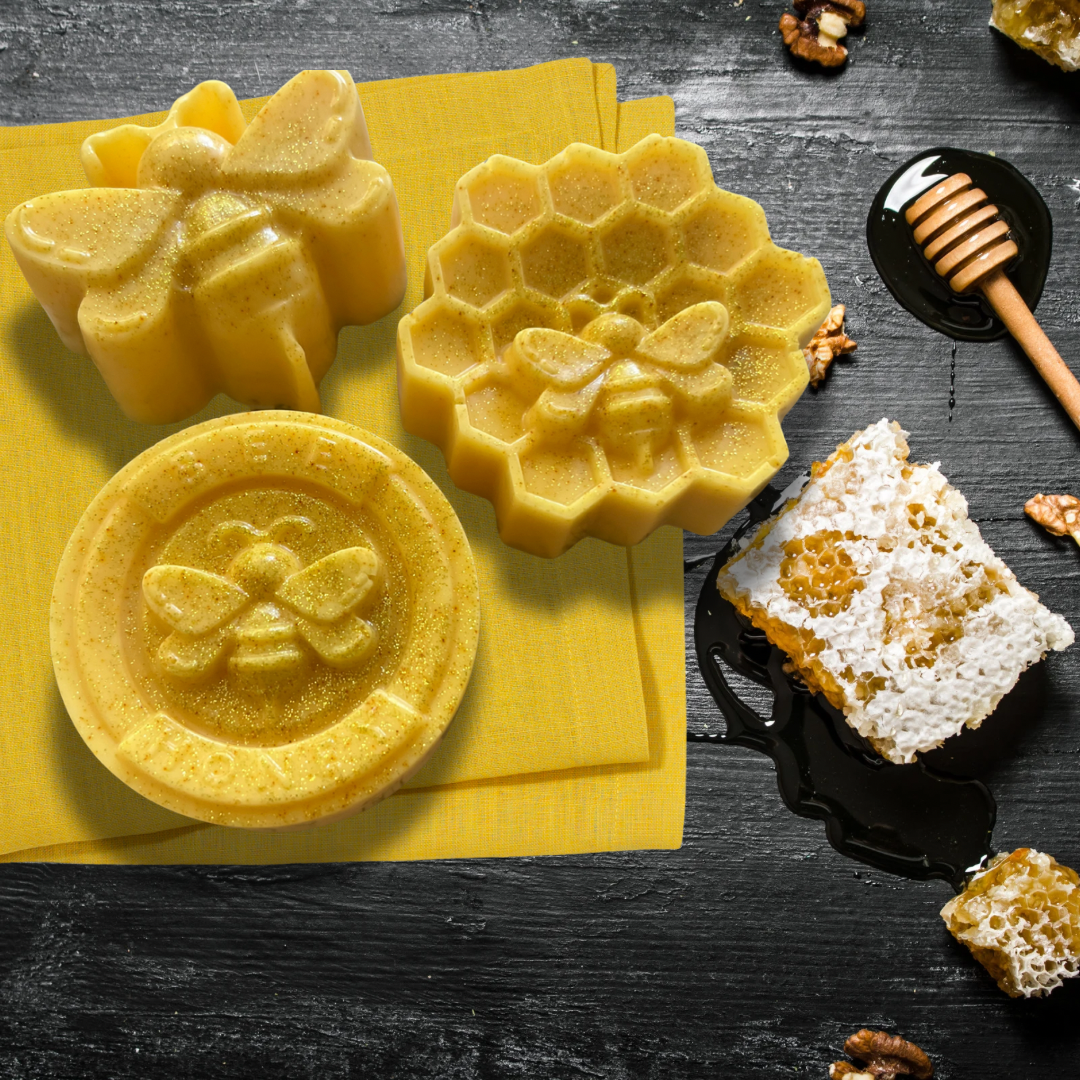 Three yellow honeycomb-shaped soaps with bee designs on a black surface with honey and honeycomb.