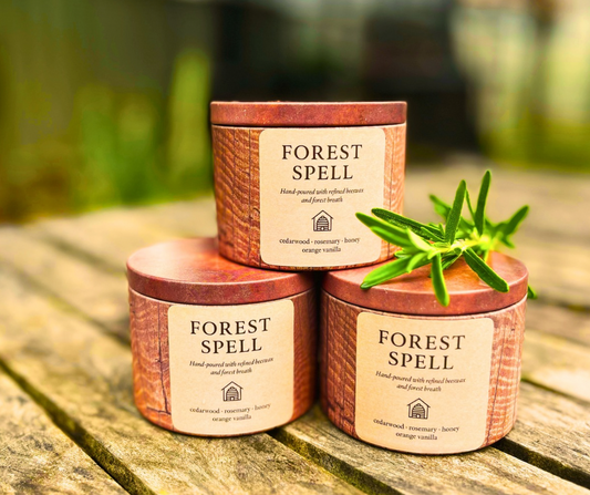 Three 'Forest Spell' candles stacked on a wooden surface with a blurred natural background
