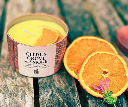 Candle labeled 'Citrus Grove & Smoke' with sliced oranges on a wooden surface
