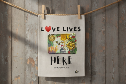 Linen tea towel with 'Love Lives Here' text and illustrations of bees, flowers, and a house.