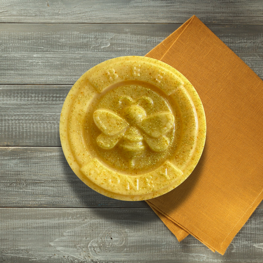Yellow soap bar with a bee design on a wooden surface with an orange napkin.